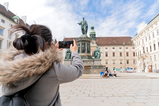 asian female woman traveller enjoy holiday vacation city walking hand using smartphone taking photo of Statue of francis ii Vienna City Hall  in the Historic City Center tour in Vienna Austria