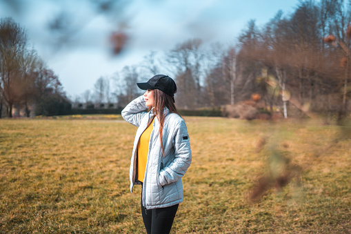 Asian mid adult female walking in a public park. Wearing a hat and enjoying sunny weather in the nature.