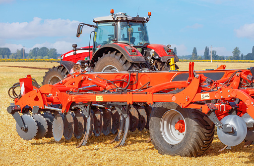 Multi-row disc harrow attached to a tractor and working on an agricultural field. The harrow consists of several rows of discs that cultivate the soil and prepare it for sowing. It is a powerful and efficient agricultural equipment.