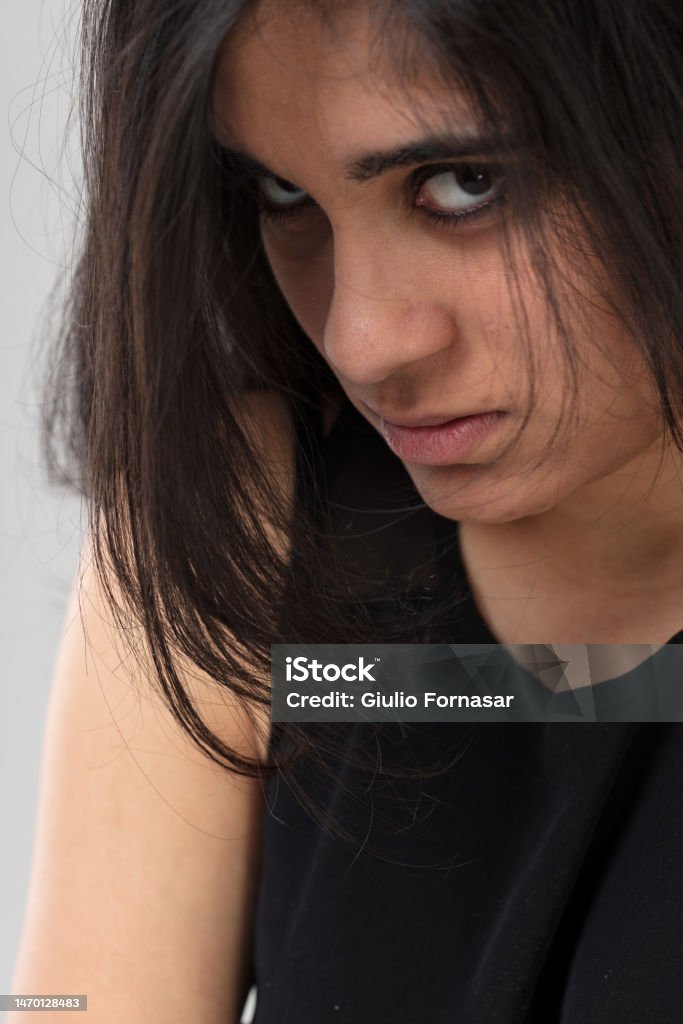 Frightened Indian girl with haunted eyes Frightened look of an Indian girl, she looks down at us and her eyes can be seen through her long hair. She looks uncomfortable, wary and resentful. It suggests violence suffered. Abuse Stock Photo