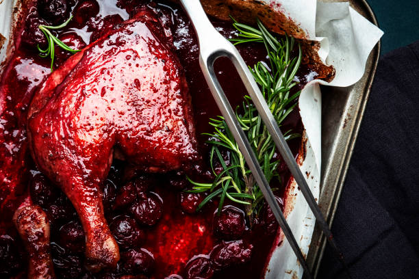 patas de pato al horno con salsa de vino tinto cereza con romero fresco en bandeja para hornear vieja. cena delicada. fondo azul de la mesa de la cocina, vista superior - animal leg duck meat chicken leg herb fotografías e imágenes de stock