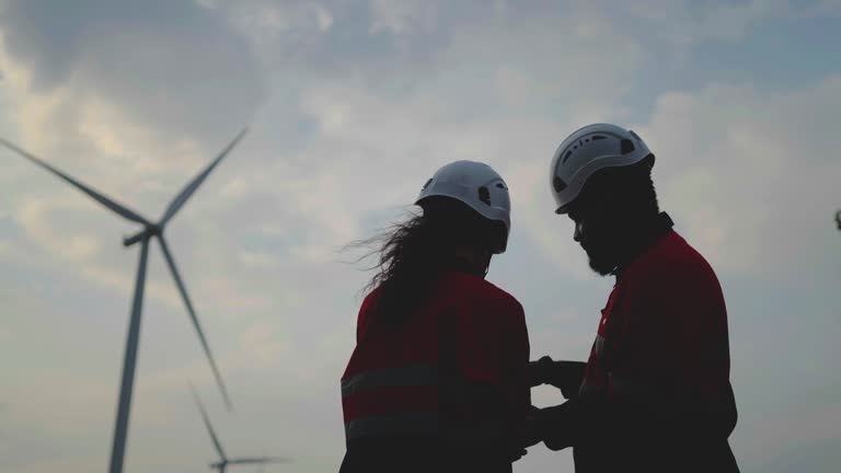 Silhouette of african american man and woman engineers in uniform discuss with laptop stand near wind turbines ecological energy industry, Environmentally friendly for the future