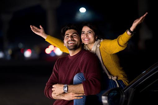 Carefree couple spending leisure time on car hood outdoors at night