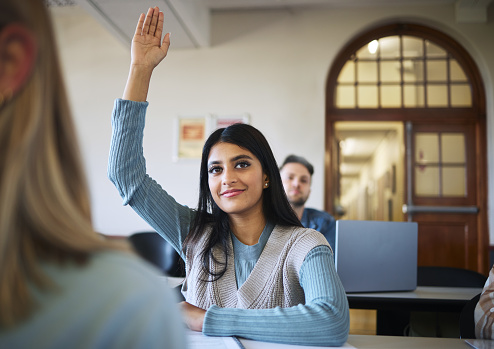 Classroom, woman and students hand for learning at university, ask question and studying for education. Indian woman, college scholarship and arm in air for course happiness at lecture hall table