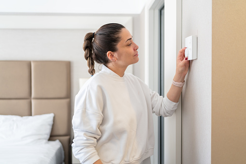 Woman Setting Temperature On Air Conditioner Control Panel In Hotel Room