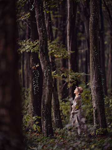 Young woman standing among trees with her eyes closed during autumn day in the forest. Photographed in medium format.