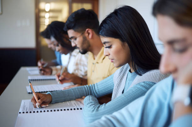 istock Students, writing exam and studying in classroom for education, university learning and test document. Young college people, knowledge and scholarship for assignment paperwork or degree information 1470142616