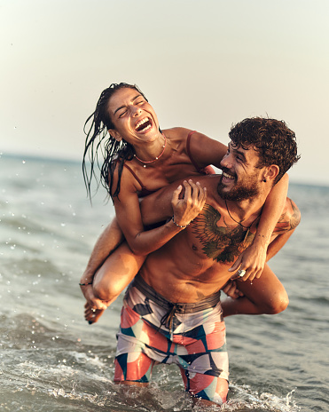 Cheerful couple having fun while piggybacking in summer day at sea. Copy space.