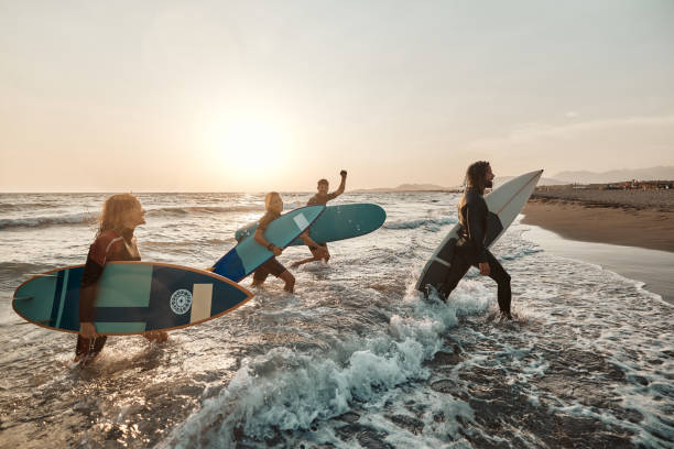 happy surfers walking out of the sea at sunset. - surfing sport extreme sports success imagens e fotografias de stock