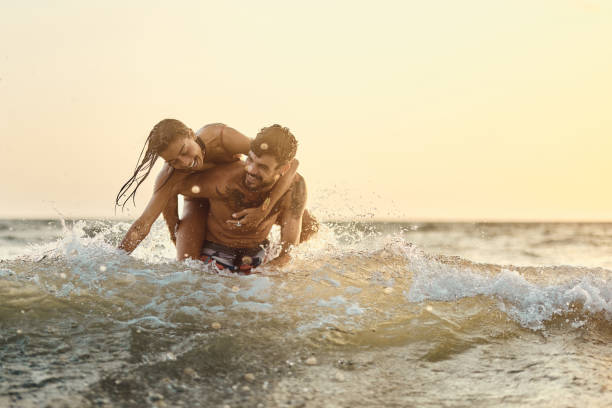 istock Cheerful couple having fun while piggybacking in sea at sunset. 1470145518
