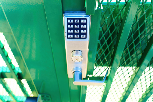 Keypad entry lock of a green fence gate outdoors, top view
