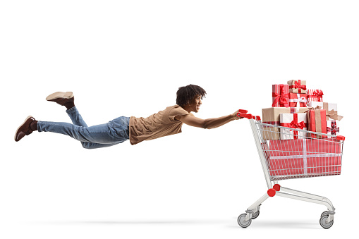 African american guy flying and holding a shopping cart full of presents isolated on white background