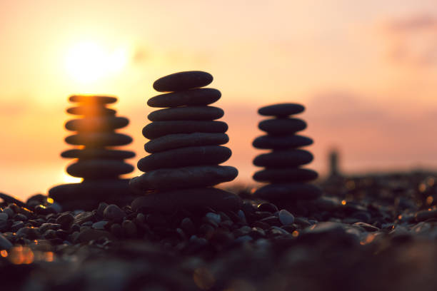 Balanced pebble pyramid silhouette on the beach at sunset. Zen stones on the sea beach, meditation, spa, harmony, calmness, balance concept.