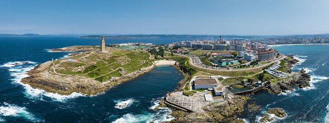 A Coruña famous ancient roman Hercules Tower - Tower of Hercules, Coastal Lighthouse and A Coruna City and Harbor Aerial Drone View from the Atlantic Ocean. Drone Point of View Stiched XXXL Panorama looking towards the famous Hercules Tower and rough atlantic ocean coast. A Coruna, Galicia, Northern Spain, Spain, Europe.