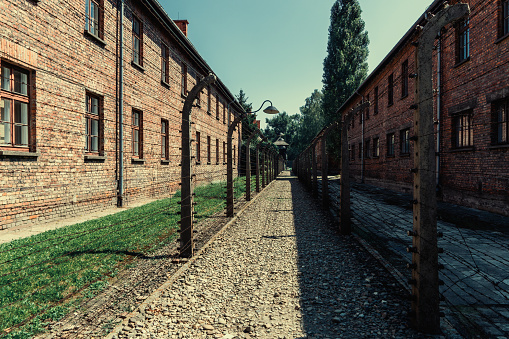 Oswiecim, Poland- 15 August 2022: Electric fence with barbed wire and brick prison buildings at the Auschwitz-Birkenau concentration camp in OÅwiÄcim, Poland. Europe.