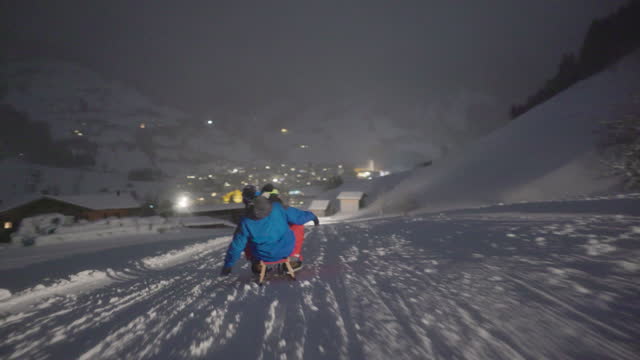 Teenagers enjoying sledding at night in a small Austrian town in European Alps