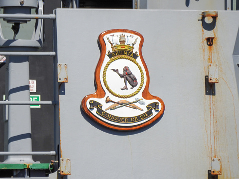 The insignia next to the bridge of HMAS Arunta, an Anzac Class frigate of the Royal Australian Navy.  She is docked at Garden Island, Sydney Harbour, in preparation for an open day to the public during Navy Week, the first open day since the Covid pandemic.  This image was taken on a sunny afternoon from Woolloomooloo Bay on 25 February 2023.