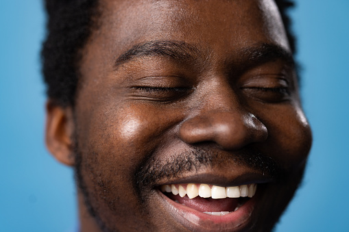Extreme close up of happy black man with toothy smile and closed eyes.