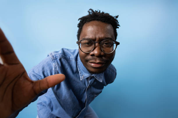 scatto in studio di un uomo nero serio in jeans su sfondo blu. - human hand palm reaching fashion model foto e immagini stock