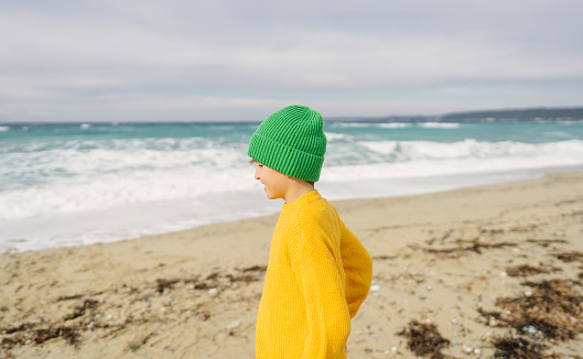 Photo of a young boy playing at the beach, by the wavy and rough sea at winter