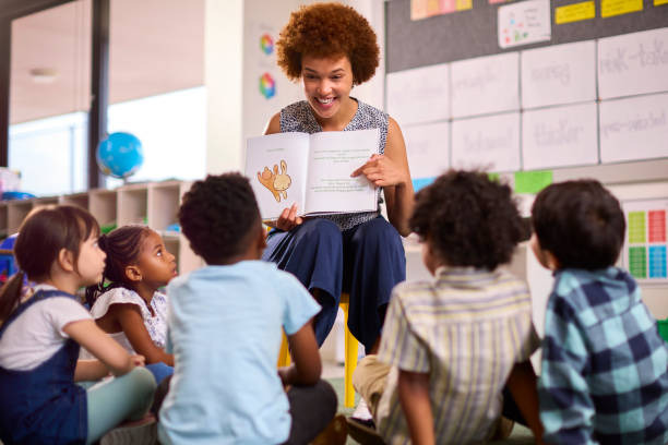 lehrerin liest multikulturellen grundschülern vor, die in der klasse in der schule auf dem boden sitzen - kind im grundschulalter stock-fotos und bilder