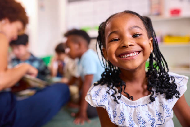 Ritratto dell'alunna sorridente della scuola elementare femminile che si siede in classe a scuola - foto stock