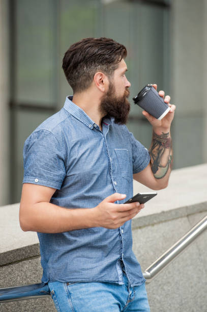istock Bearded guy texting via mobile phone while drinking coffee outdoors Chatting online on mobile device 1470160451