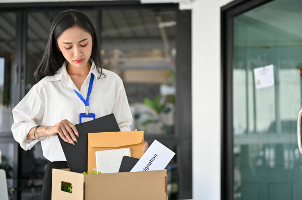 istock Sad Asian female office worker packing her stuff into a cardboard box, being fired from her boss. 1470160570