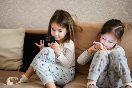 Two sisters wear pajamas playing phones early in morning.