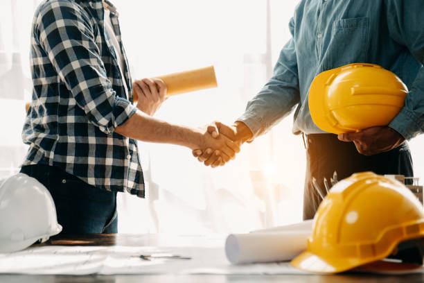 istock Construction team shake hands greeting start new project plan behind yellow helmet on desk in office center to consults about their building project. 1470161615