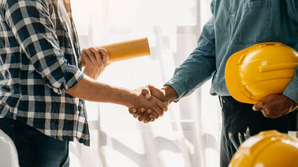 el equipo de construcción se da la mano saludando el inicio del nuevo plan de proyecto detrás del casco amarillo en el escritorio en el centro de oficinas para consultar sobre su proyecto de construcción. - contratista de obras fotografías e imágenes de stock