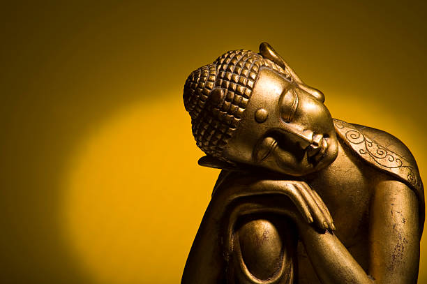 A resting Buddha statue on a gold shadowed background stock photo