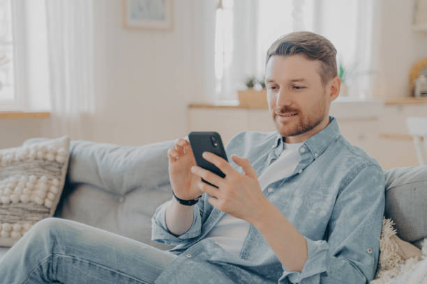 istock Young man sitting on couch and surfing web on his phone 1470164199