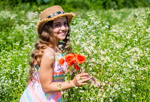 Girl in a hat and dress with a bouquet of poppies in a poppy field