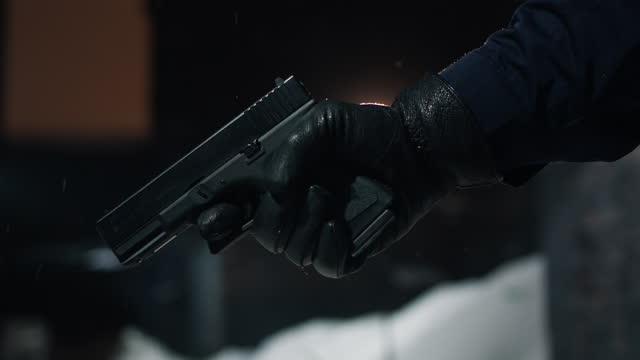 A gloved hand with a pistol is raised in the frame