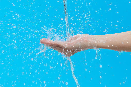 Close up of woman hand under flowing water on blue background.