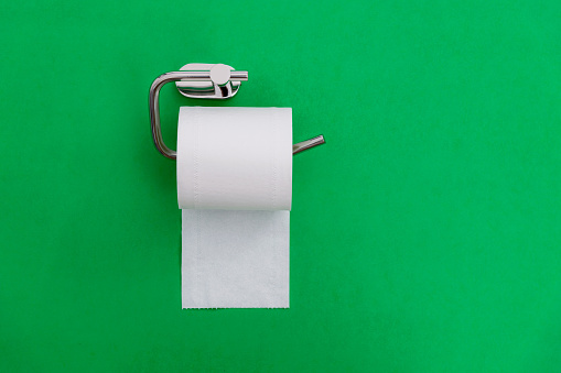 Roll of white toilet paper hanging on green background.
