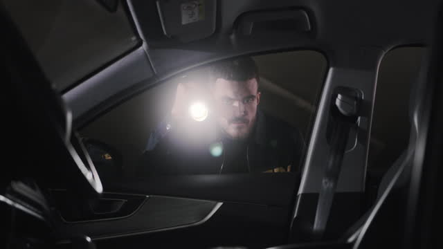 An FBI agent with a flashlight inspects the car through the door in search of physical evidence