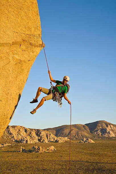 A rock climber rappelling past an overhang in Joshua Tree National Park, California, on a summer evening.