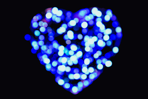 Defocused blue and white circles of light in the shape of a heart with bokeh effect on a black background