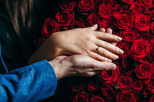 Hands of men and girl with wedding ring red flowers background