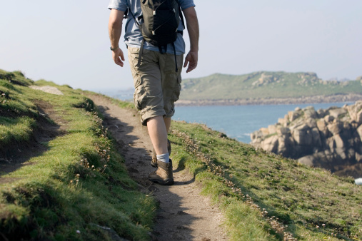 A man walking along a coastal path in Cornwall, UK.