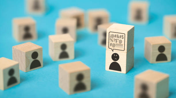 Angry person surrounded by a group of people Front view of a group of  wooden cubes with icons representing persons. The main focus is on an angry person who has a cube over his head with a thought bubble full of insults rudeness stock pictures, royalty-free photos & images
