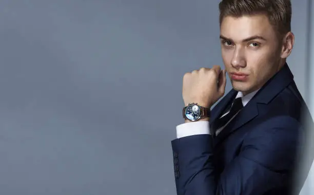 Photo of Portrait of an elegant handsome businessman in a classic blue suit on a gray background with copy space