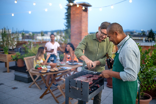 Two friends grilling beef on barbecue grill on urban garden.
