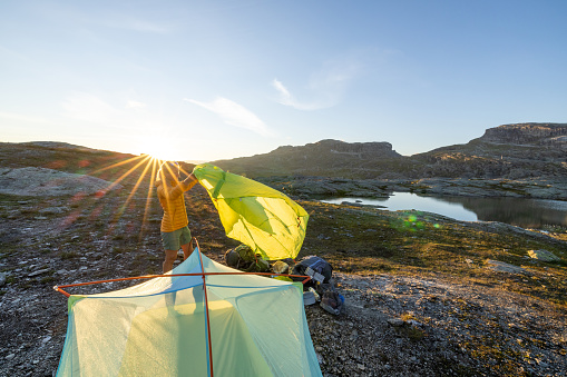 She builds up her shelter at sunset before dark. Wild camping in the mountains in Norway in summer.