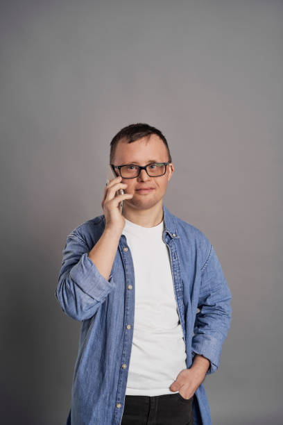 Adult man with down syndrome talking by mobile phone on gray background stock photo