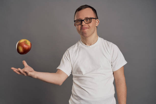 istock Man with down syndrome throwing up apple in hands on gray background 1470200246