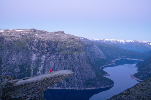 Male hiker standing on Trolltunga (troll tongue) famous rock high above a lake with panoramic view of the valley, popular tourist adventure trek in Norway