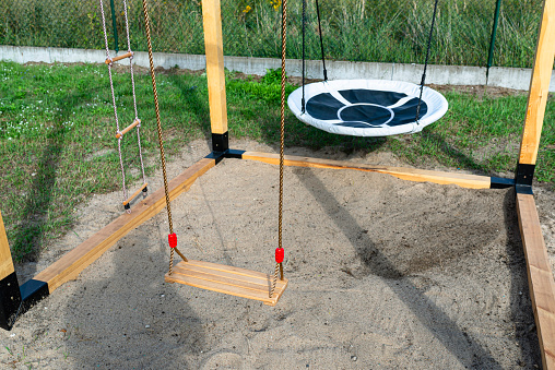 A modern cubic playground made of wooden logs and metal corners, a visible rocker and a nest.